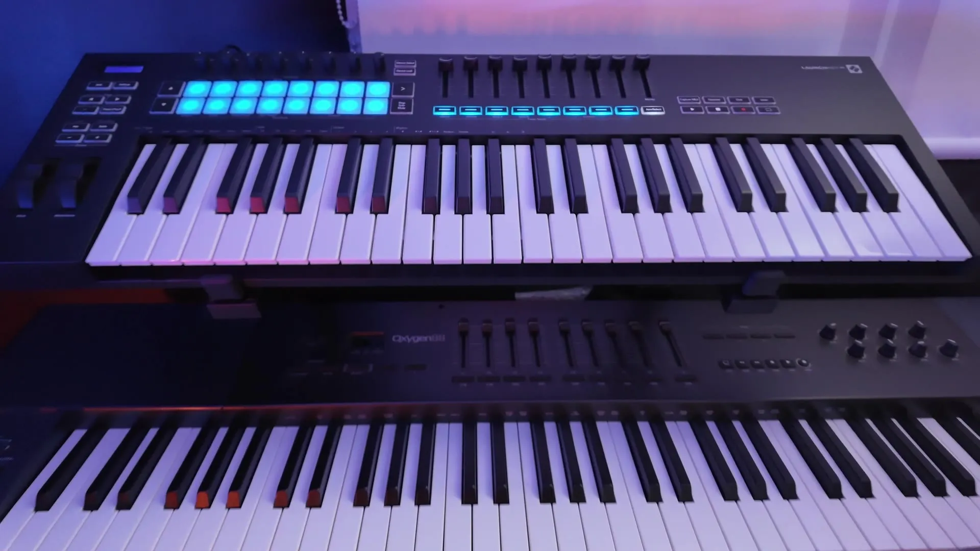 A Novation Launchkey with lit pads, stacked above a larger keyboard controller