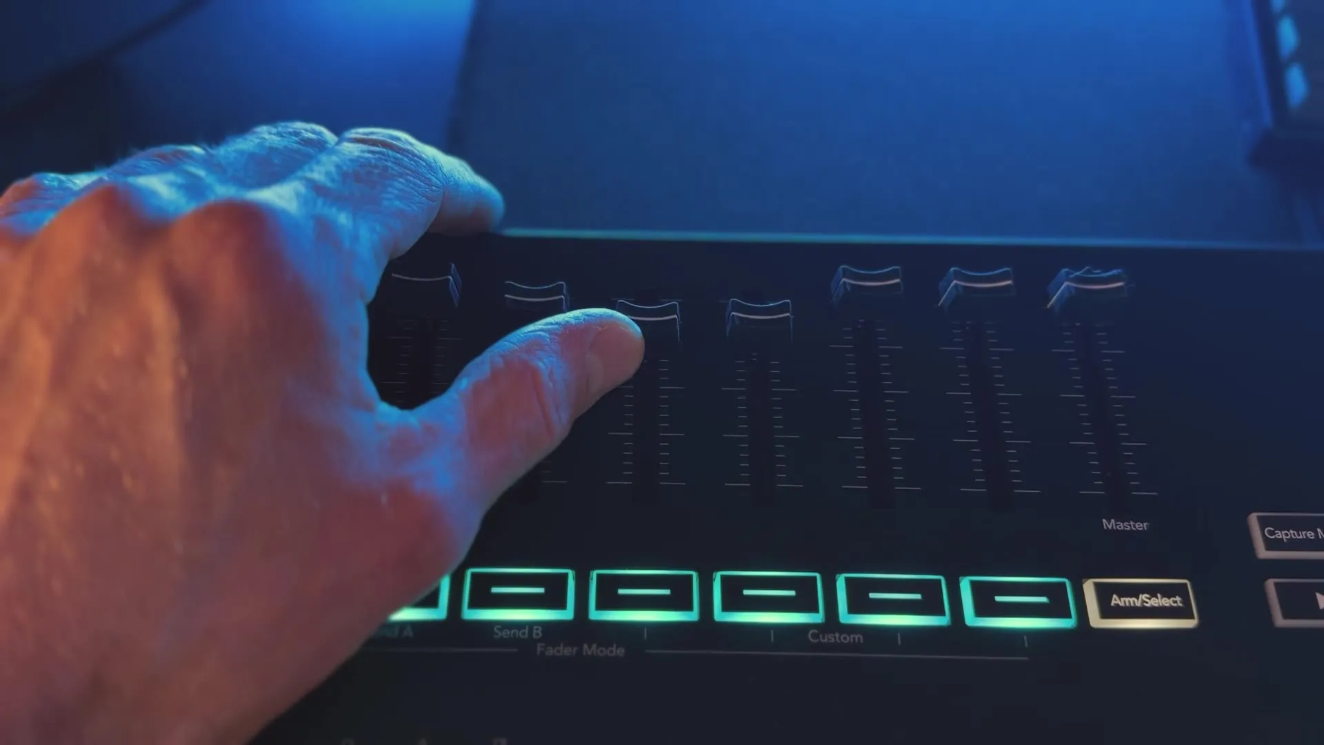 A hand moving the faders on a Novation Launchkey, lit in blue